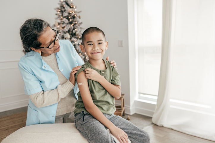 Boy Vaccinated during Winter Holidays. Nurse is standing  near Christmas Tree