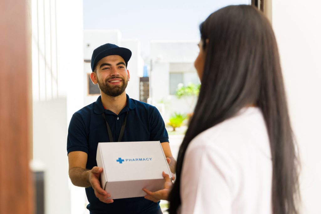 Friendly delivery man is handing a box with prescription medication to a woman at her front door
