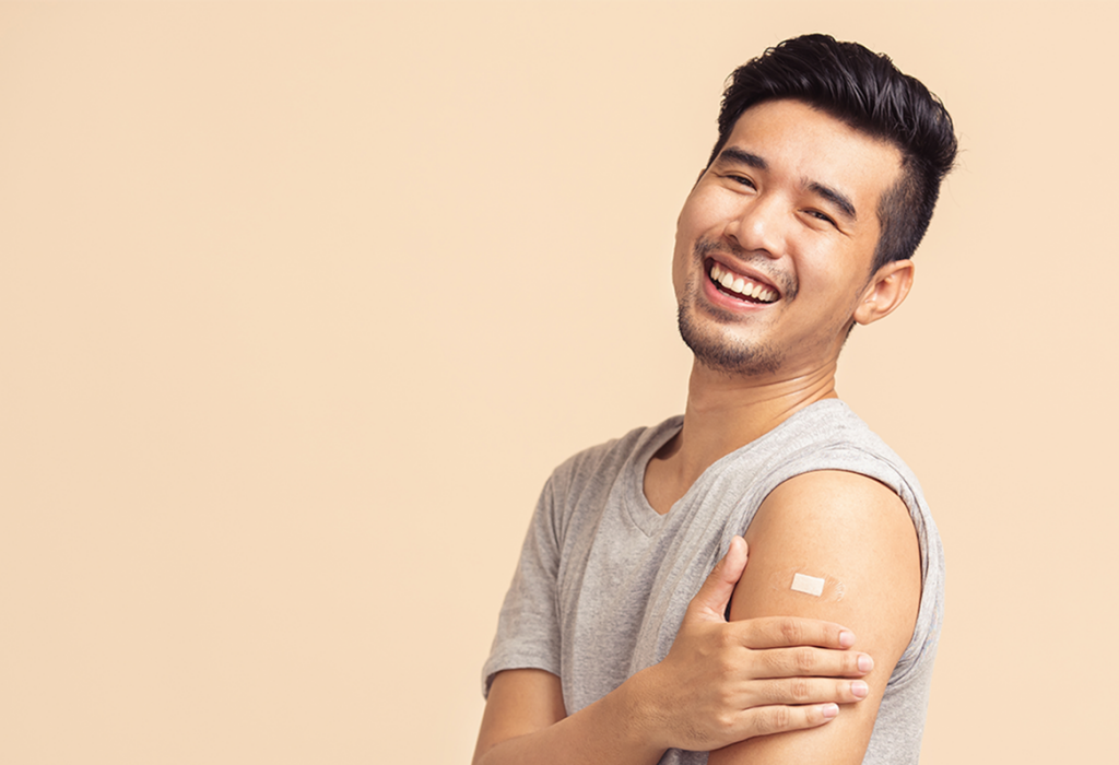 asian holding up shirt to show vaccine bandaid